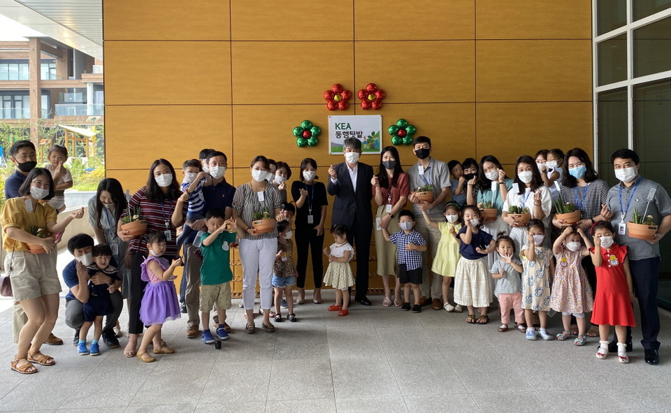 지난 3일 에너지공단 본사에서 진행된 ‘동행텃밭’ 조성 행사에 참석한 김창섭 이사장(현판 앞 회색 정장)이 사내 어린이집 원생, 가족들과 함께 기념촬영을 하고 있다.